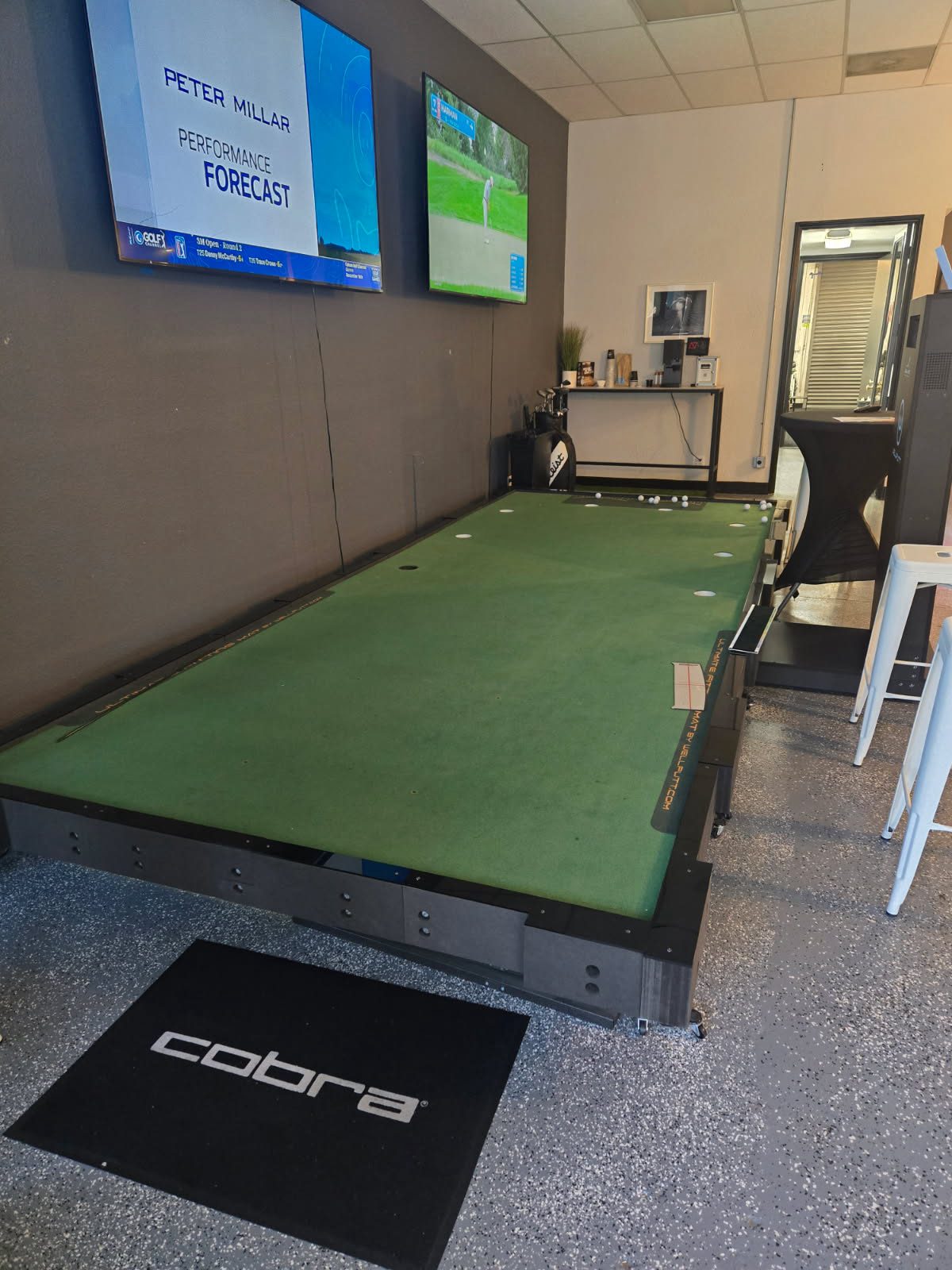The raised putting green inside NB2 with TVs on the wall above